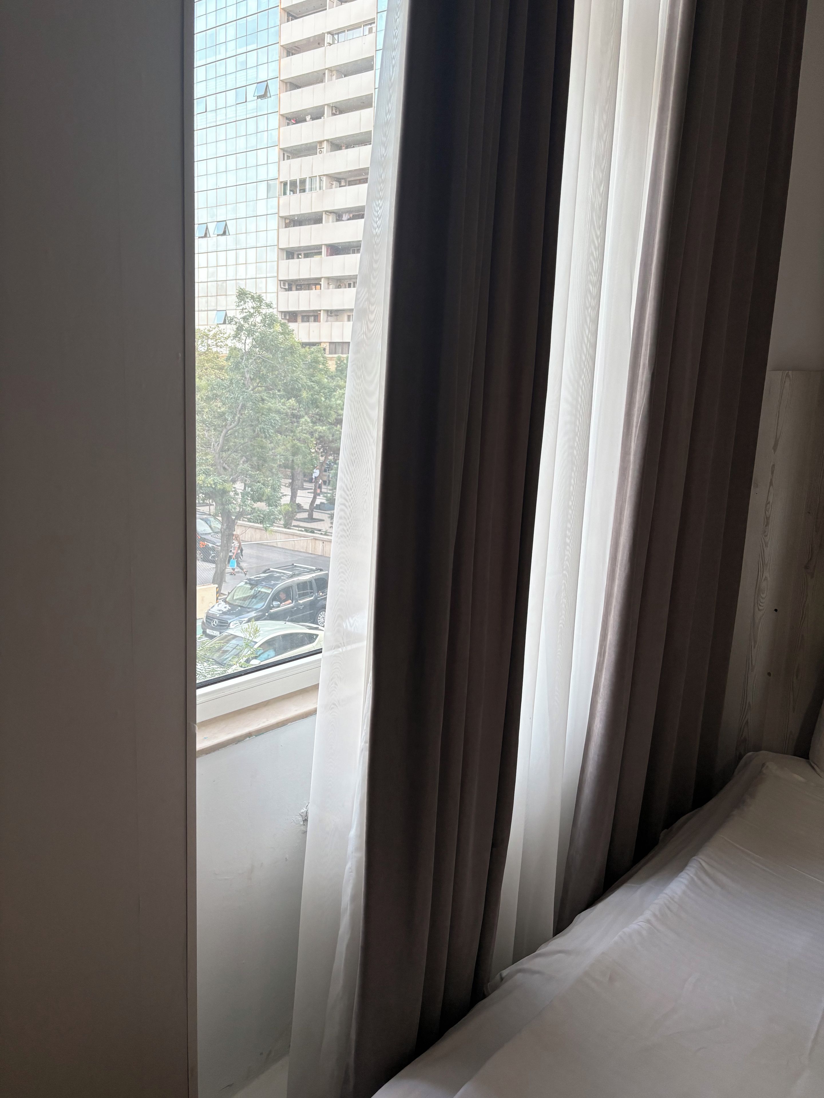 Une chambre d’hôtel avec vue sur le paysage urbain, visible à travers de fines rideaux.