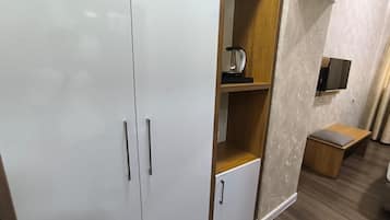 A room with a wardrobe, a small cabinet, a television mounted on the wall, and a wooden bench.
