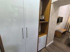 A room with a wardrobe, a small cabinet, a television mounted on the wall, and a wooden bench. - Empire Hotel Baku (Baku)