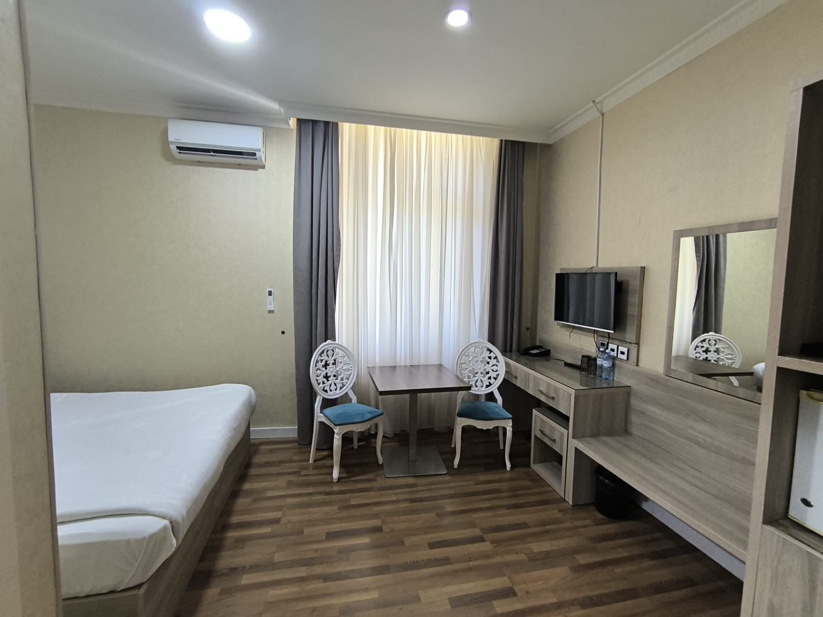 Una camera d'albergo con un letto, una scrivania con una sedia, una televisione e una finestra con tende.