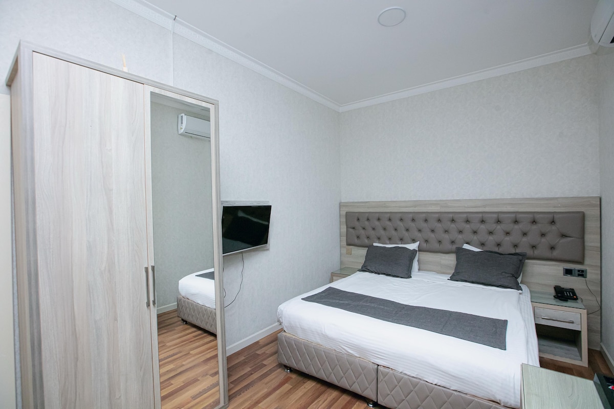 A bedroom with a bed, a television mounted on the wall, a bedside table with a phone, and a wardrobe.