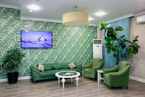 A living room with a green sofa, two armchairs, a coffee table, a TV mounted on the wall, and a large potted plant. - Empire Hotel Baku (Baku)