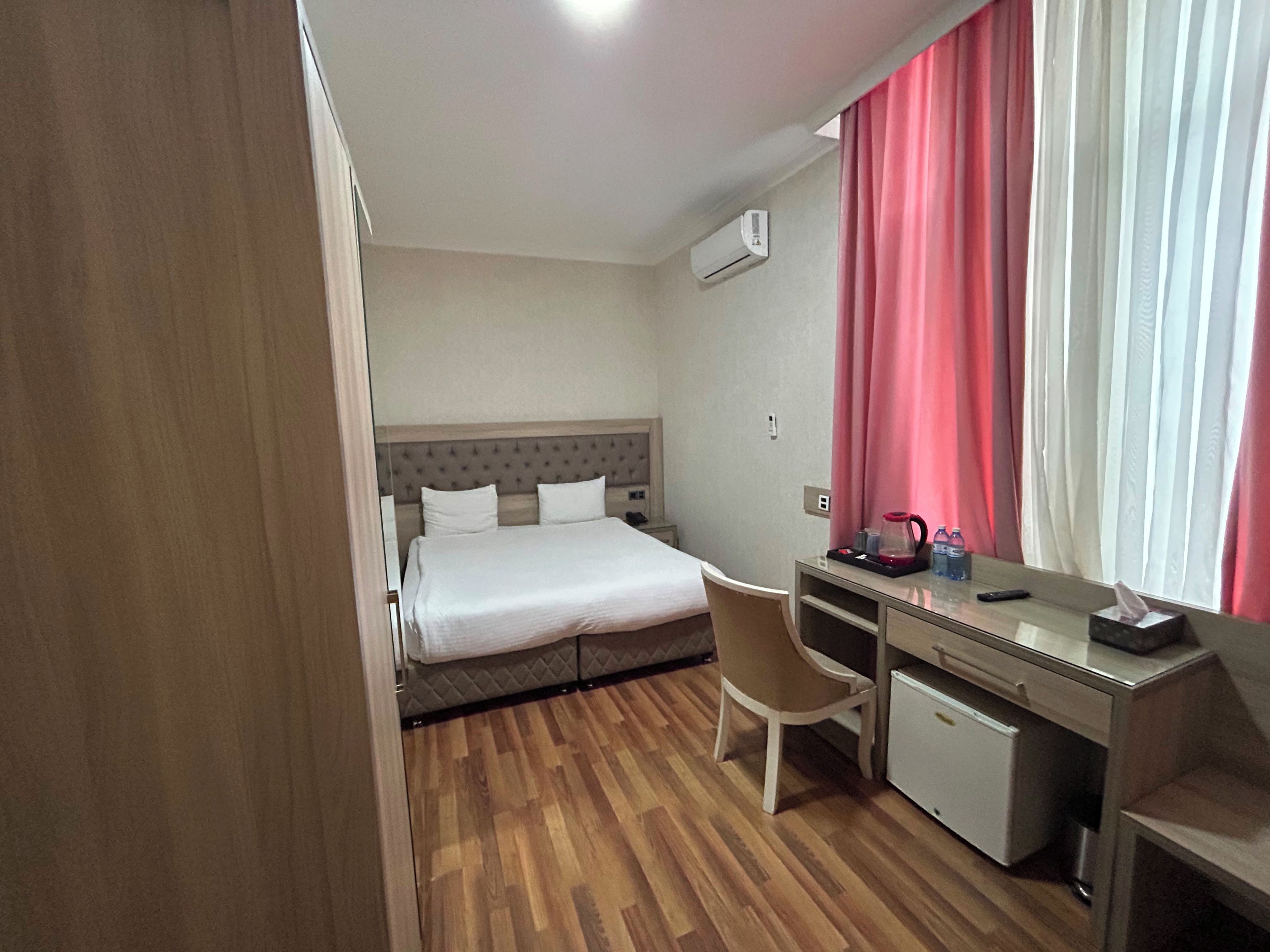 Habitación de hotel con cama, escritorio, silla, aire acondicionado y ventana con cortinas.