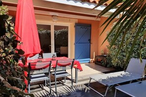 An outdoor patio with a table and chairs, a blue door, and a covered area with a red umbrella. - Comfortable atmosphere at the bathing lagoon (Gruissan-Les Ayguades)