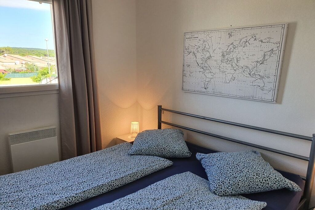 Un lit simple avec un cadre en métal, une carte accrochée au mur et une fenêtre avec des rideaux.