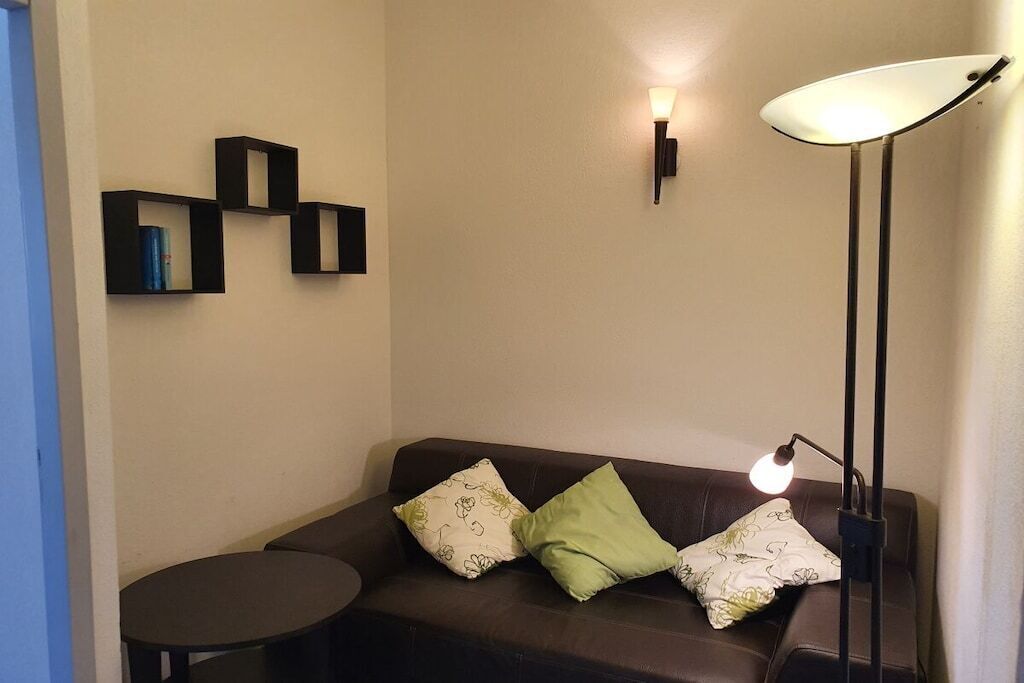 A room with a brown leather sofa, two pillows, a small round table, and a floor lamp.