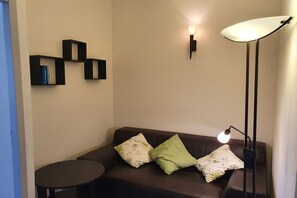 A room with a brown leather sofa, two pillows, a small round table, and a floor lamp. - Comfortable atmosphere at the bathing lagoon (Gruissan-Les Ayguades)