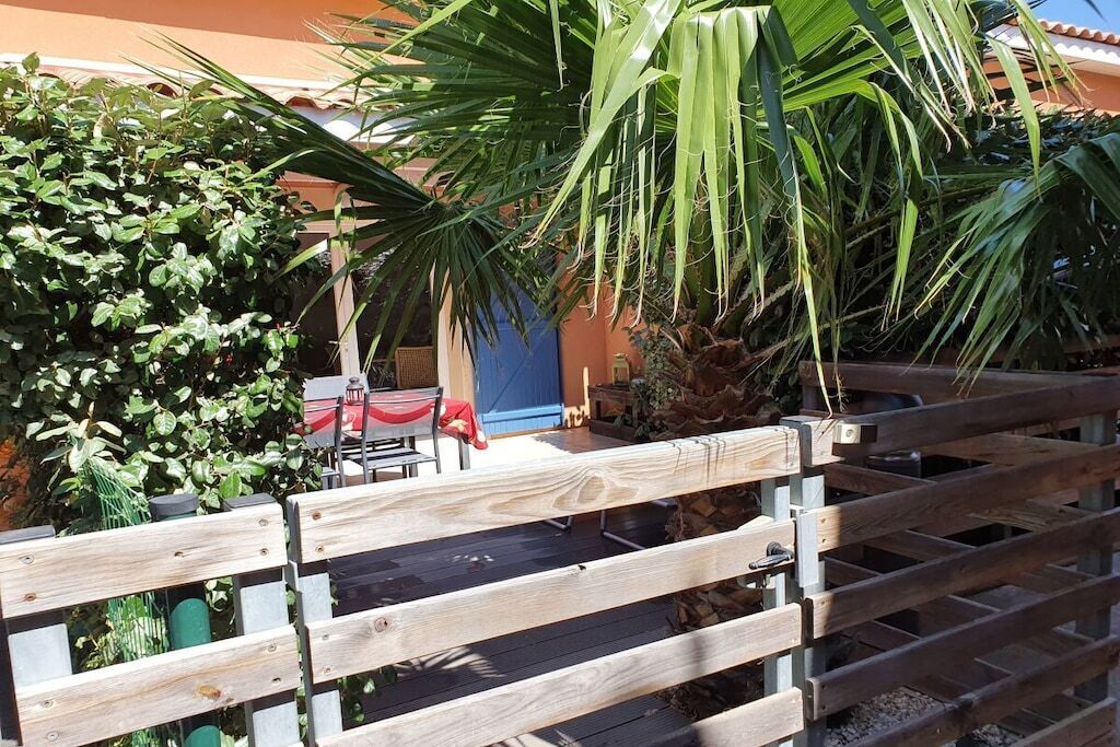 Een houten hek met een poort, een palmboom en een gebouw met een blauwe deur op de achtergrond.