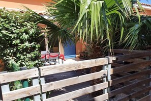 A wooden fence with a gate, a palm tree, and a building with a blue door in the background. - Comfortable atmosphere at the bathing lagoon (Gruissan-Les Ayguades)