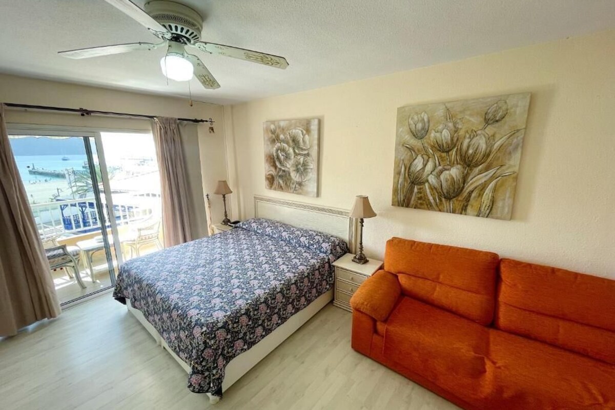 A bedroom with a bed, a sofa, a ceiling fan, and artwork on the walls.