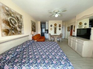 A bedroom with a bed, a chair, a table, a television, and a ceiling fan. - Edificio Arco (Arona)