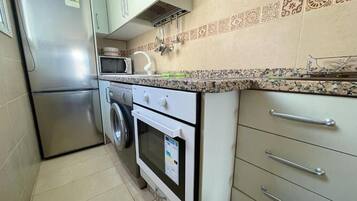Una cocina compacta con refrigerador de acero inoxidable, microondas, lavadora y estufa.