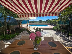 Uma área externa coberta com piscina, uma mesa de madeira com cadeiras e um vaso de flores.