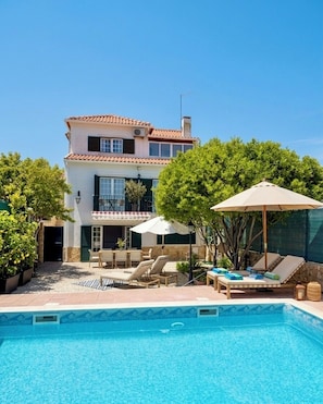 Uma casa de dois andares com piscina, área de estar ao ar livre e um terraço coberto.