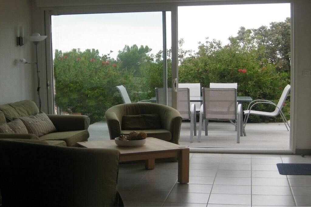 A living room with a sofa, a coffee table, and a view through a sliding glass door to an outdoor patio with a table and chairs.