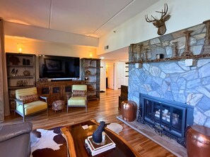 A living room with a stone fireplace, a television, and a bookshelf. - Welcome to your mountain getaway! 2 bedroom condo is located on the 8th floor (Sugar Mountain)