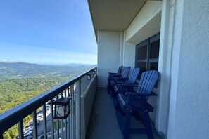 Varanda com vista para uma paisagem montanhosa, com várias cadeiras Adirondack e um corrimão.