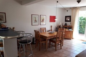A dining area with a wooden table and chairs, a bar counter with stools, and a kitchen area with cabinets and a sink. - Sun villa with roof terrace (Narbonne-Plage)