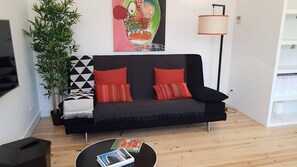 A modern living room with a black sofa, red cushions, a round coffee table, a floor lamp, and a large abstract painting. - Duplex near the Arch (Lisboa)