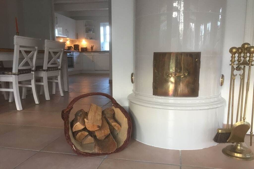 Ein Wohnzimmer mit Kamin, ein Essbereich mit weißen Stühlen und eine Küche im Hintergrund.