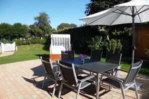 Eine Terrasse im Freien mit Tisch, Stühlen, einem weißen Sonnenschirm und einem Grill.