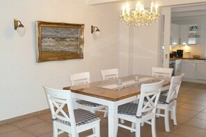 Un coin repas avec une table en bois et des chaises blanches, un lustre et un tableau encadré au mur.