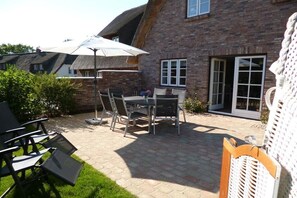 Une terrasse avec une table et des chaises, un parasol blanc, et un bâtiment en briques doté d’une fenêtre et d’une porte.