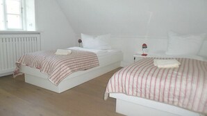 Quarto com duas camas de solteiro, janela com veneziana listrada e radiador.