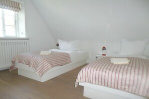 Ein Schlafzimmer mit zwei Einzelbetten, einem Fenster mit gestreifter Vorhangzierde und einer Heizung.
