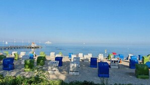 Uma praia com fileiras de cadeiras de praia numeradas e guarda-sóis, um píer ao fundo, e o mar.