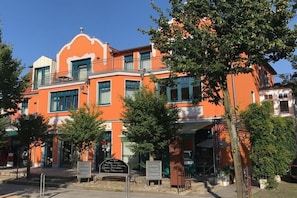 Ein mehrgeschossiges Gebäude mit einer leuchtend orangefarbenen Fassade, Balkonen und einer Schautafel davor.