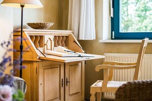 Une pièce avec un bureau en bois, une chaise, une lampe et une fenêtre donnant sur un paysage verdoyant.