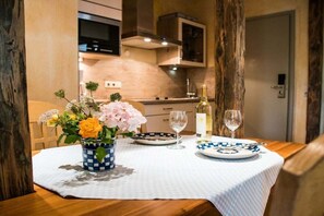 A dining table set with a vase of flowers, plates, and wine glasses in a room with wooden furniture and a kitchen in the background. - Tower House Holiday Apartment 6 (Kühlungsborn)
