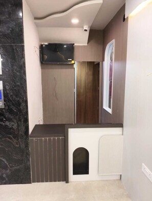 A room with a marble floor, a wooden door, a white radiator, and a small black dog house. - ANJU VILLA (Varanasi)