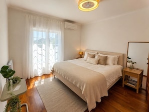 A bedroom with a bed, bedside table, and a window with curtains. - Casa Forever Young — Perfect 4-Bedroom House with Pool in Fabulous Sesimbra (SESIMBRA)