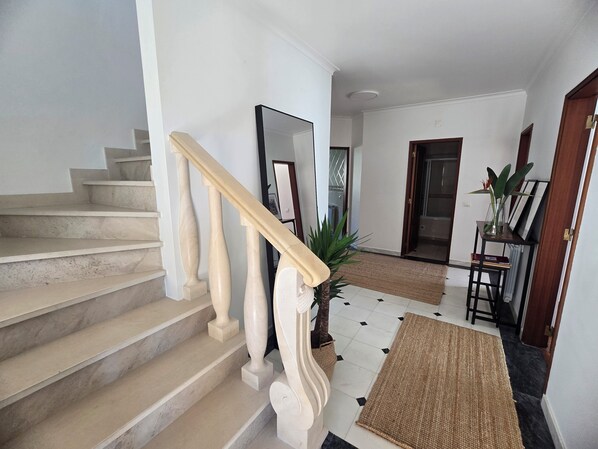 Una escalera con escalones de mármol y balaustradas de madera que conduce a un rellano con un espejo y una planta.