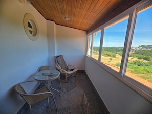A balcony with a table and two chairs, a wooden ceiling, and a view of greenery and buildings. - Casa Forever Young — Perfect 4-Bedroom House with Pool in Fabulous Sesimbra (SESIMBRA)
