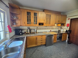 Una cocina con armarios de madera, un lavamanos de acero inoxidable, lavavajillas y cafetera.