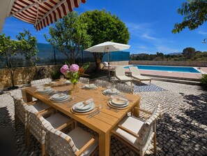 Un área de comedor al aire libre con una piscina de fondo.