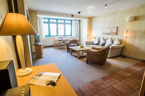 A living room with a sofa, a coffee table, a wicker chair, a lamp, and a television. - Tower House Holiday Apartment 5 (Kühlungsborn)