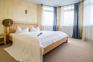 A bedroom with a wooden bed, white bedding, a bedside table, and a wall-mounted light fixture. - Tower House Holiday Apartment 5 (Kühlungsborn)