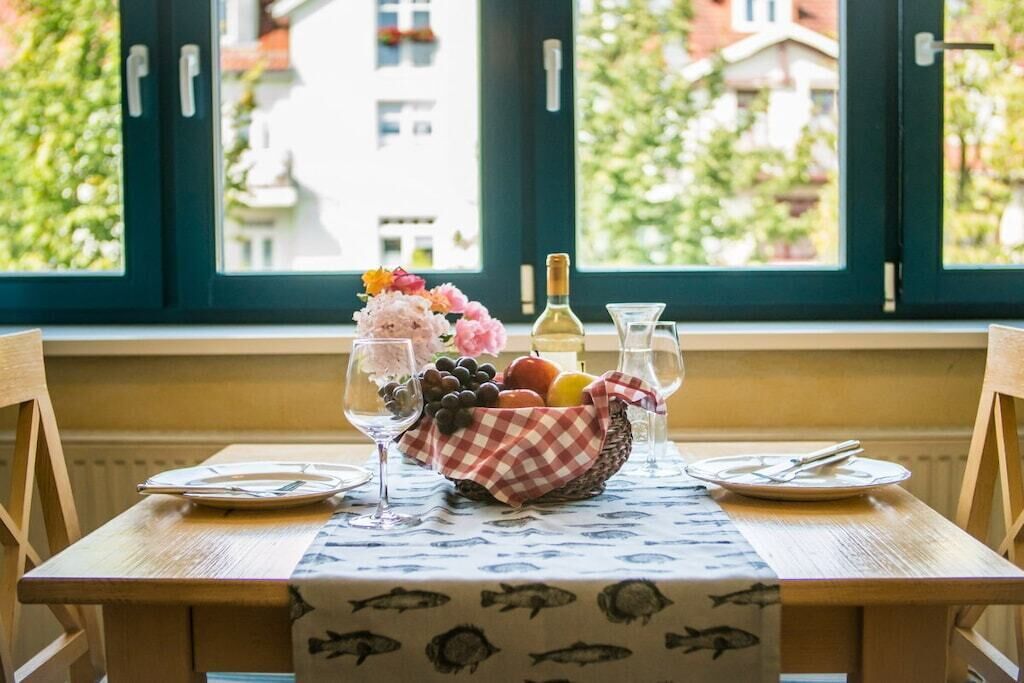 A dining table with a checkered tablecloth, a fruit basket, wine glasses, and plates set for two.