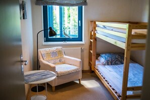 Habitació petita amb un llit superposat, una cadira, un escriptori i una finestra que dona a zona verda.