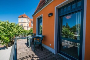 A balcony with a table and chairs, a large window, and a building in the background. - Tower House Holiday Apartment 4 (Kühlungsborn)