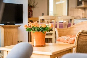 Ein Wohnzimmer mit Fernseher, einem Tisch mit Blumenvase und einem Essbereich mit Stühlen und Tisch.