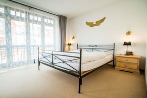 A bedroom with a metal-framed bed, two bedside lamps, a wooden nightstand, and a wall-mounted decorative piece. - Tower House Holiday Apartment 3 (Kühlungsborn)
