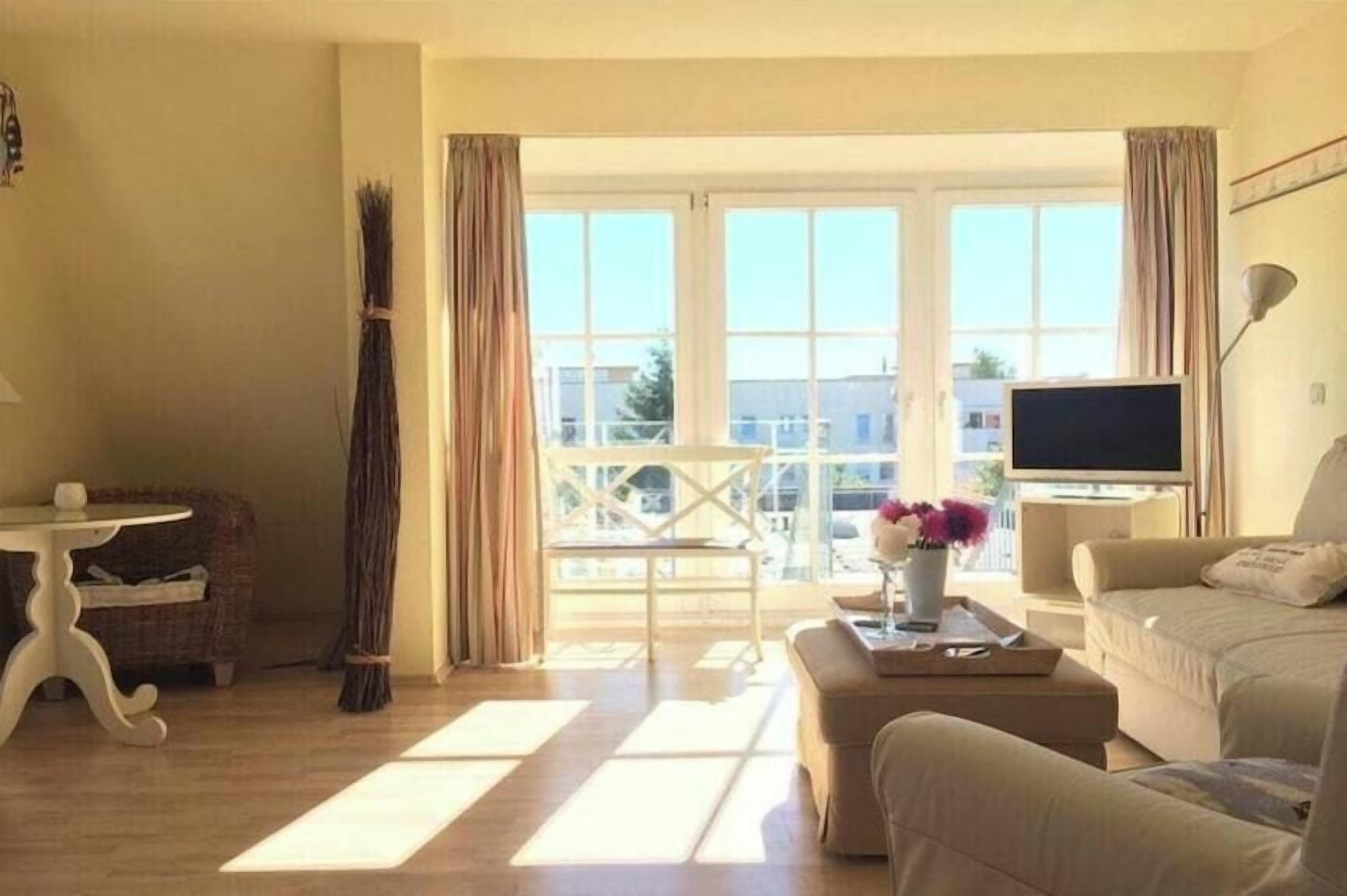 Una sala de estar con sofá, mesa de centro, televisor y ventana con cortinas.