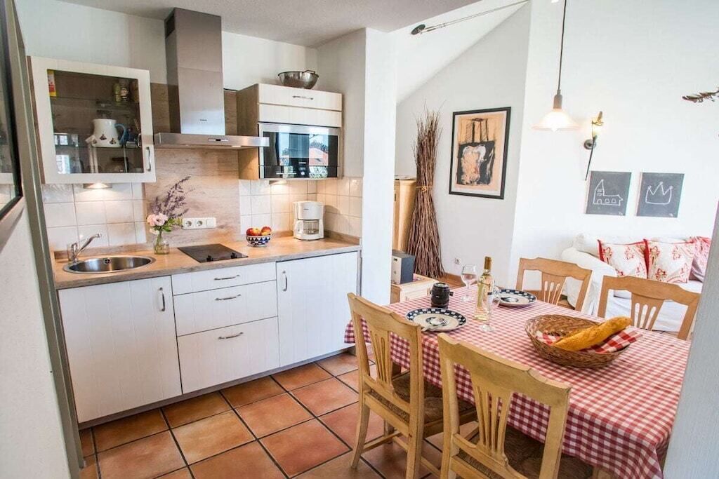 A compact kitchen with a sink, stove, and microwave. There is a dining table with chairs and a red checkered tablecloth.