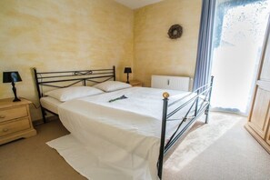 A bedroom with a bed, bedside tables, a radiator, and a window with curtains. - Tower House Holiday Apartment 8 (Kühlungsborn)
