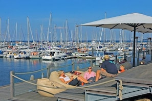 A marina with multiple boats docked, a wooden deck with a lounge chair, and a clear view of the water. - Tower House Holiday Apartment 8 (Kühlungsborn)